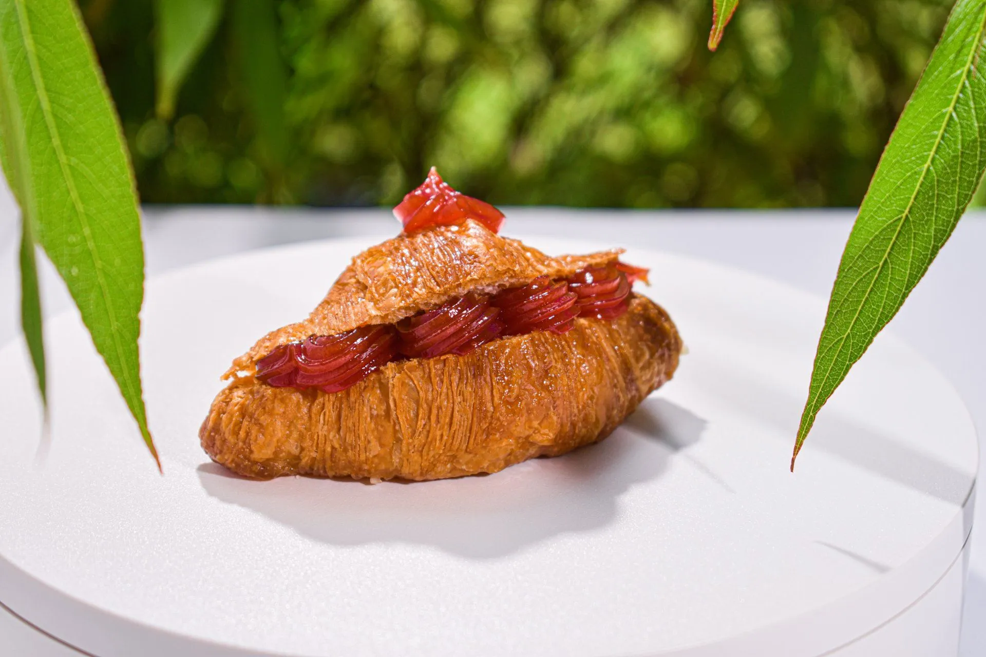 Croissant relleno de fresa sobre un plato blanco, entre hojas verdes