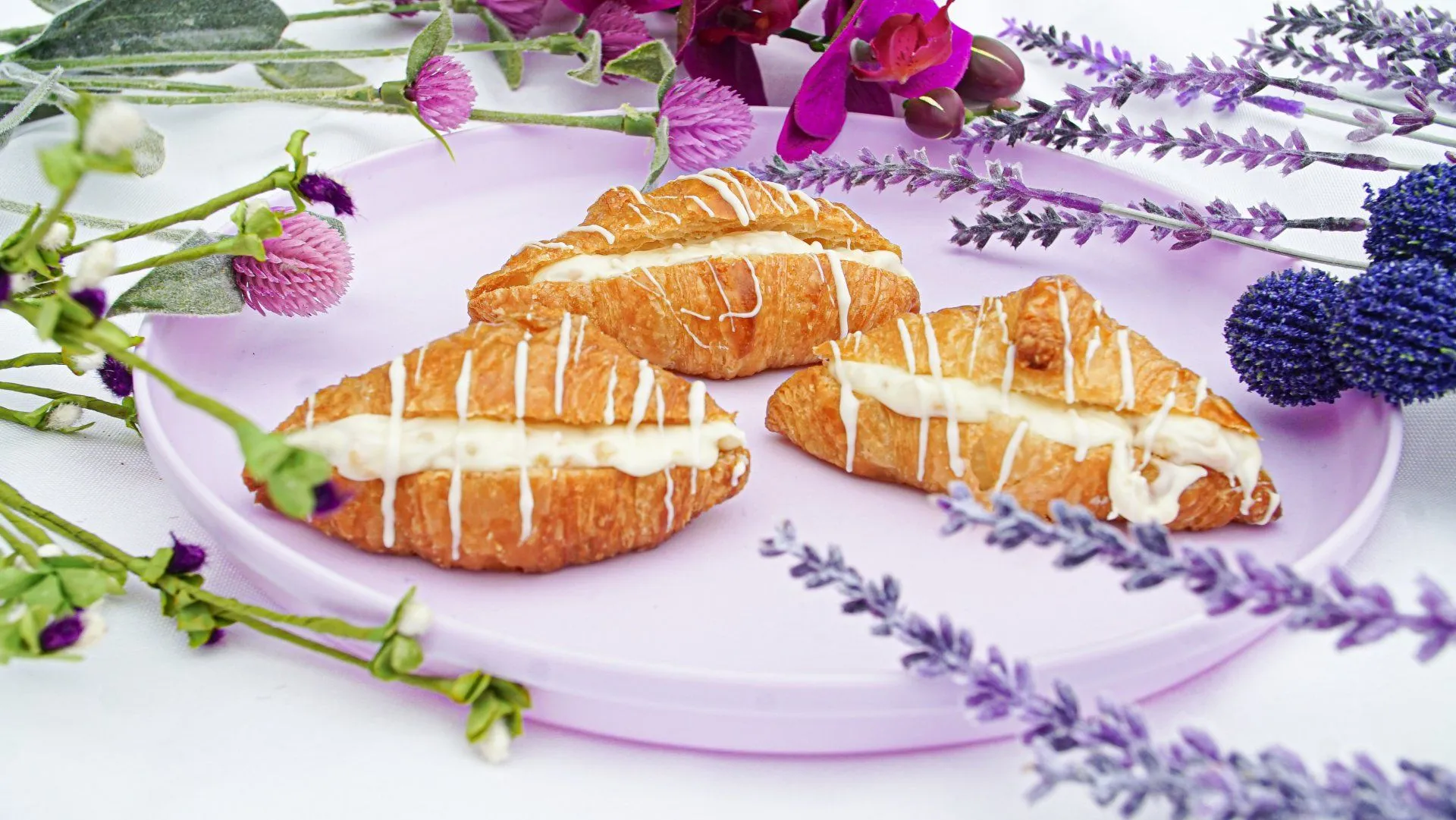 Croissants rellenos con glaseado, decorados sobre un plato entre flores